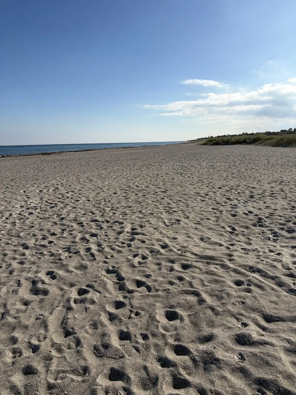 Den brede sandstrand syd for Grenaa Havn med fodspor i sandet og Kattegat i baggrunden